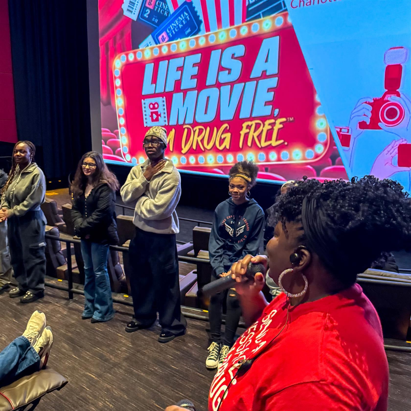 Angennetta Boyd stands at the front of theater with student ambassadors who filmed and directed their videos.